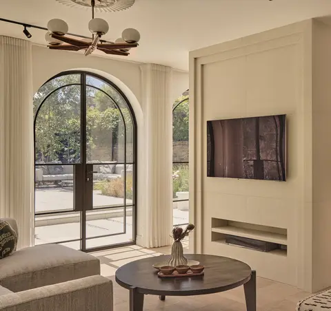 Living room with arched black steel doors to the garden, limewashed walls and a round dark-wood coffee table