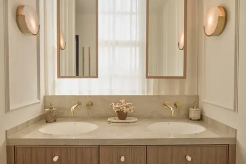 Main bathroom with a stone double vanity, brushed-brass wall taps, twin mirrors and alabaster wall lights