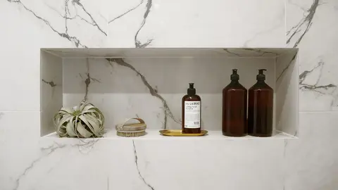 Marble-lined bathroom niche styled with amber glass bottles and air plants