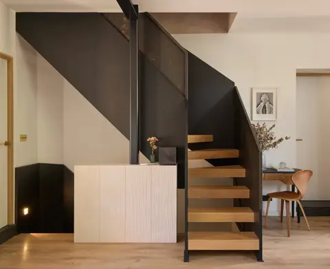 Open-tread oak staircase with a black steel stringer above a fluted cream kitchen island