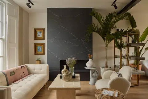 Reception room with a black marble fireplace wall, tufted cream sofa, bouclé armchair and tall palms