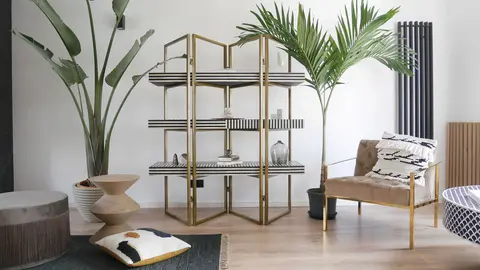 Saul shelf used as a room divider beside palms and a black armchair